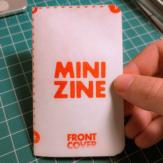 Hand holding a mini zine with 'MINI ZINE' text on a green cutting mat.
